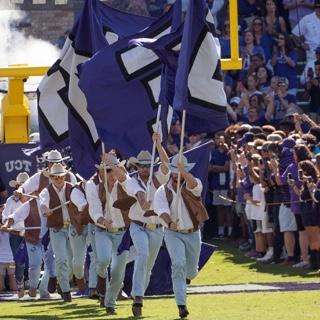 Dressed like cowboys, 的 TCU 游骑兵队 run with large flags at a football game